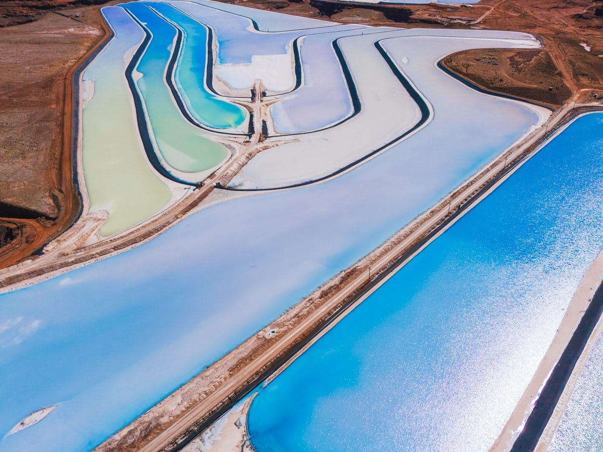 Aerial close-up of Moab’s potash evaporation ponds, showing vivid shades of blue, turquoise, and green outlined by white salt borders in the middle of the red desert.