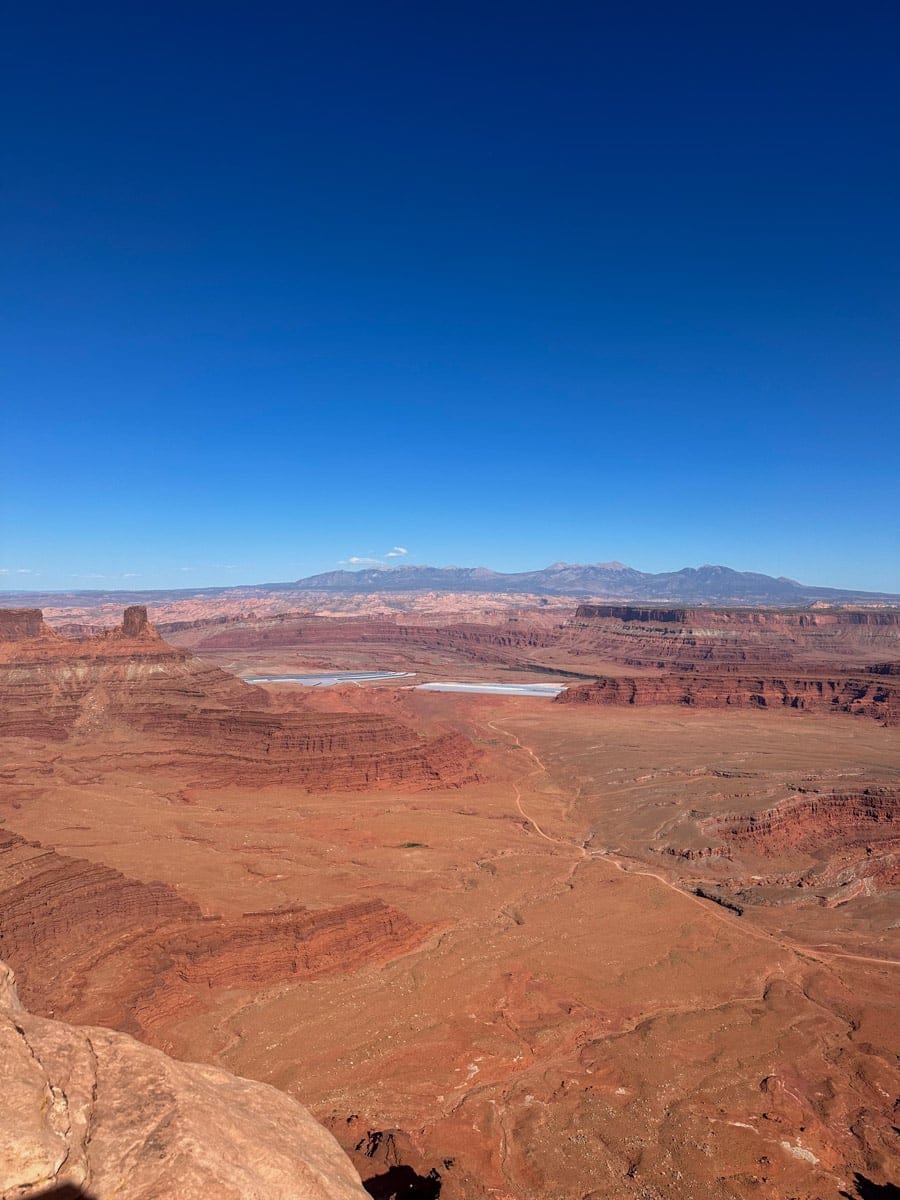 Sweeping view of Dead Horse Point State Park, with layers of red mesas, winding canyons, and distant mountains under a clear blue sky.