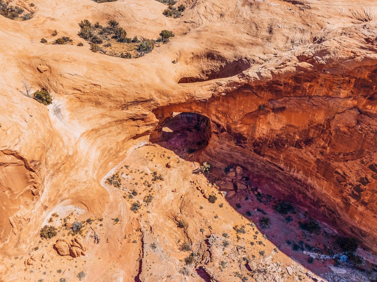 Aerial view of Pinto Arch nestled in the red rocks near Moab, Utah, surrounded by desert terrain and steep sandstone cliffs.