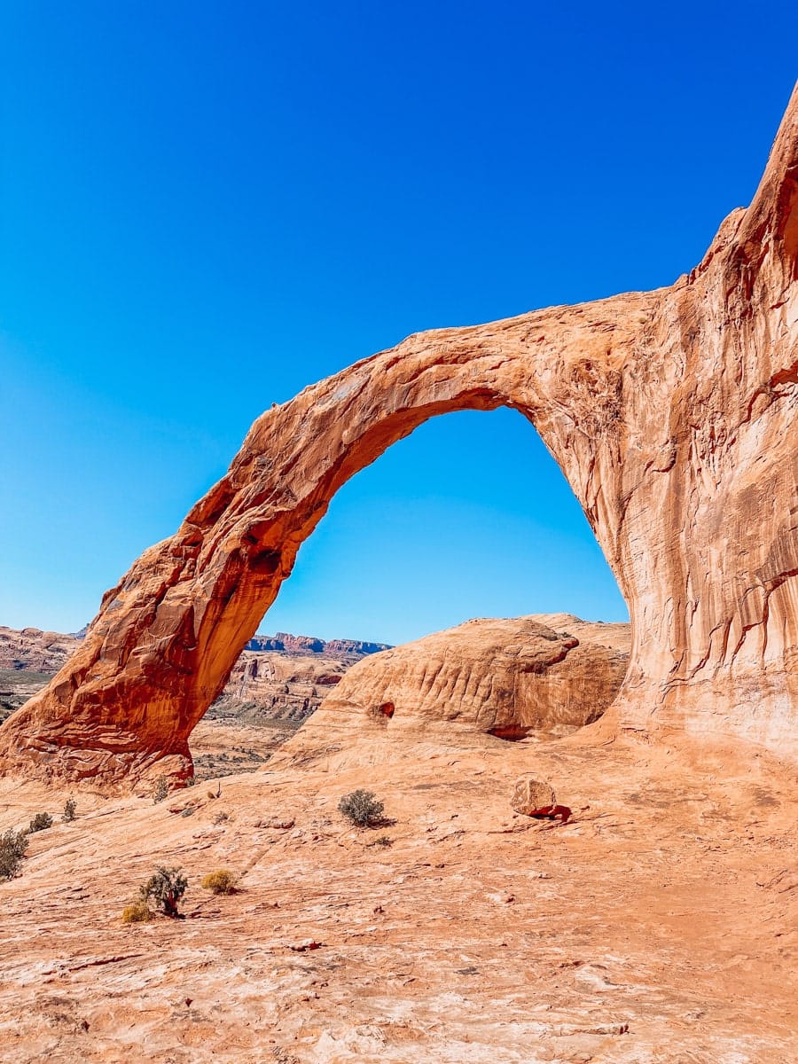 Aerial view of Corona Arch nestled in the red rocks near Moab, Utah, surrounded by desert terrain and steep sandstone cliffs.