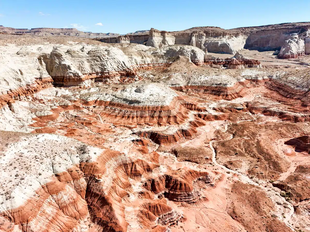 Aerial view of the colorful layered rock formations and striped hills of Paria Canyon in Utah, showcasing deep red, orange, and white hues in the desert landscape.
