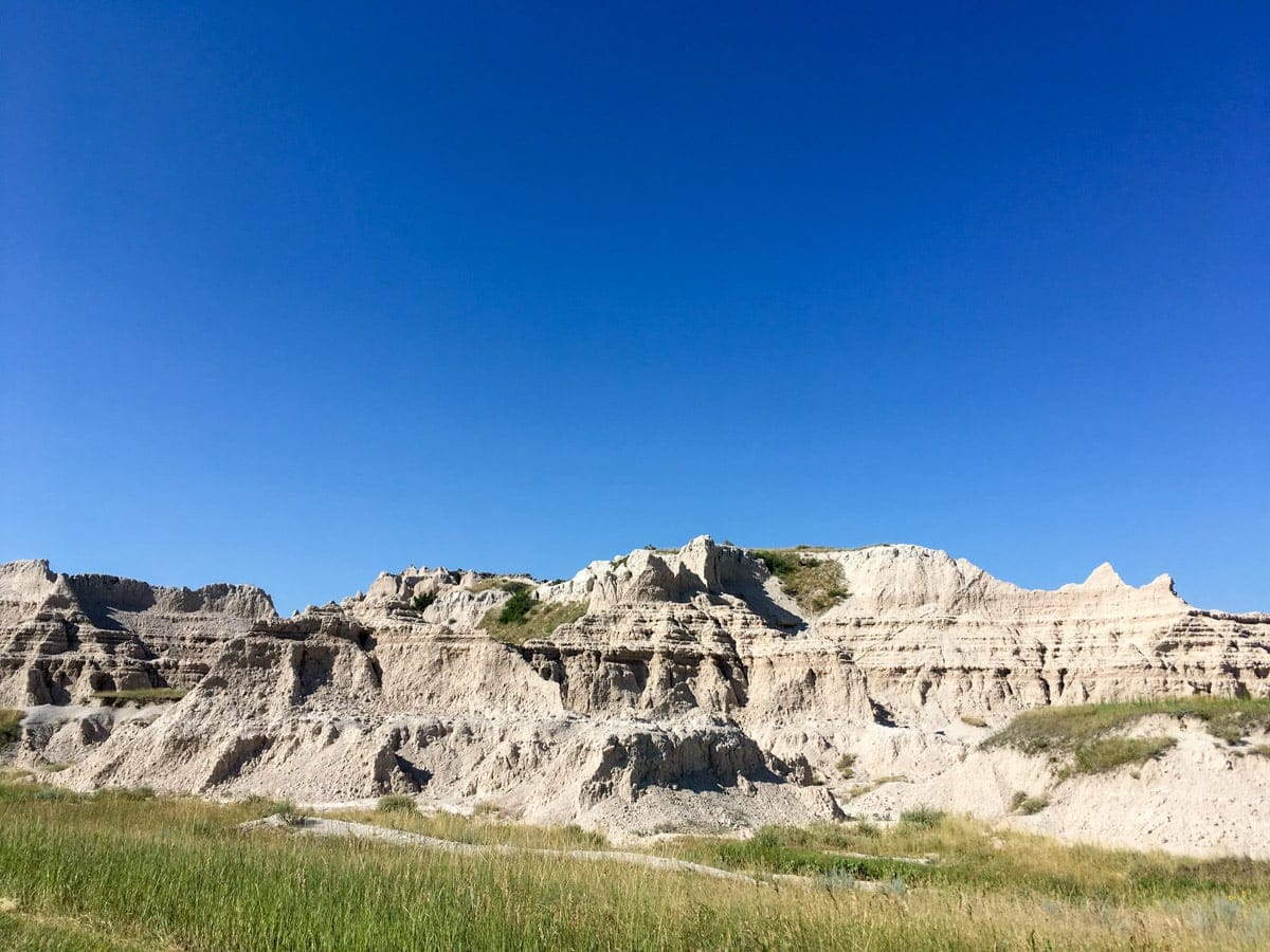 Layered rock formations in Badlands National Park under a clear blue sky, showcasing dramatic erosion and unique sedimentary textures.