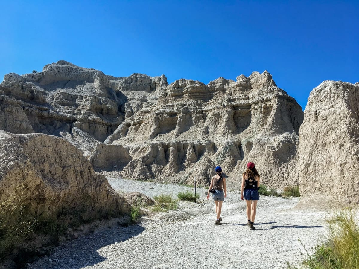 Two hikers walking along the scenic Notch Trail, framed by towering rock formations and a vibrant blue sky.