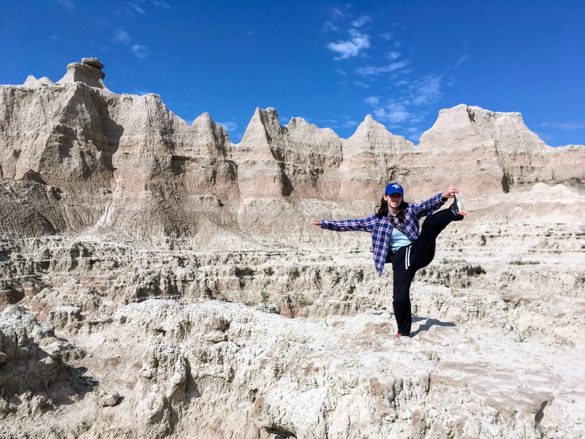 Young woman striking a playful pose among jagged rock spires while exploring off-trail at the Door Trail in Badlands National Park.