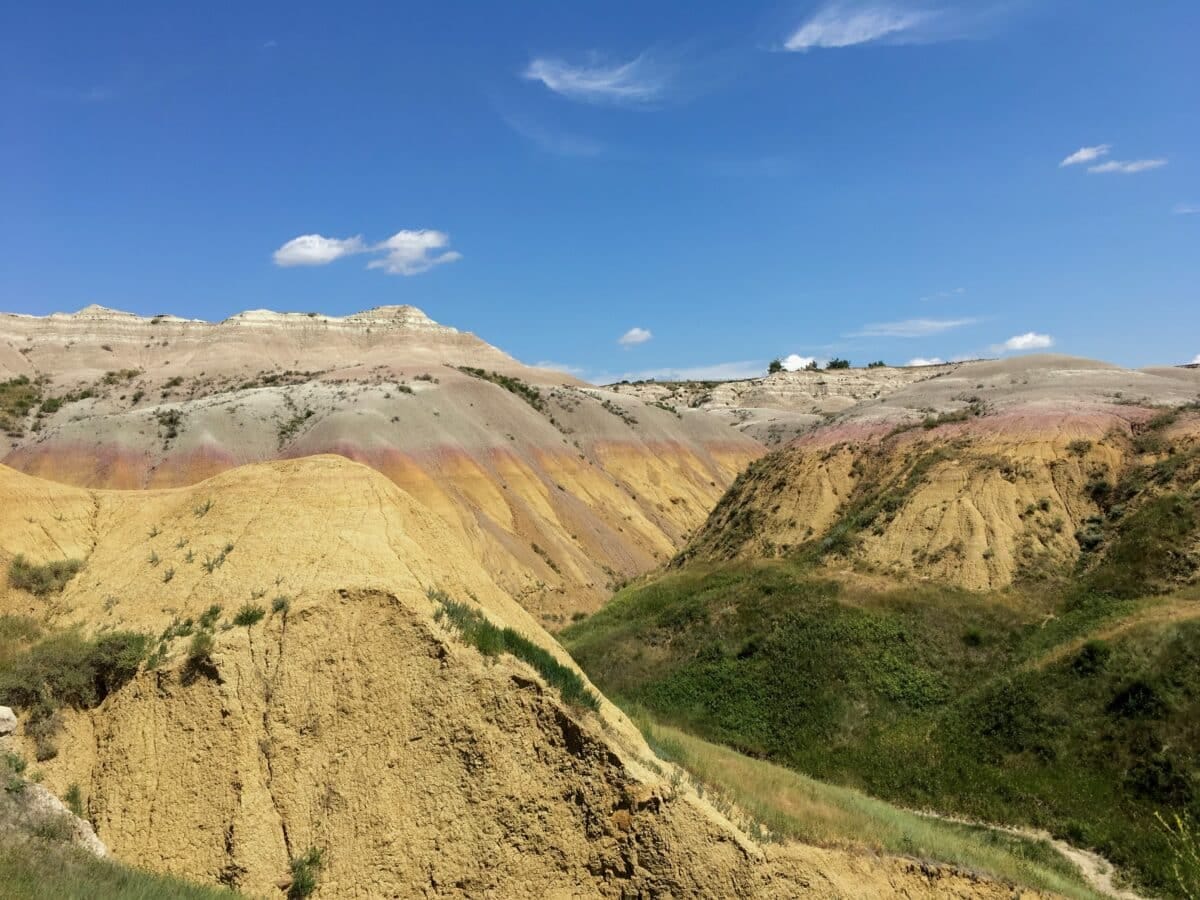 Colorful hills at Yellow Mounds Overlook, with rich layers of yellow, purple, and gray sediment contrasting against green grasses and blue skies.