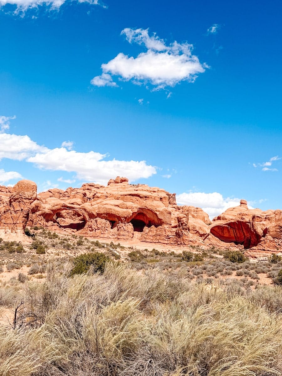 Scenic roadside view of towering red rock formations framed by a wooden fence in Arches National Park.