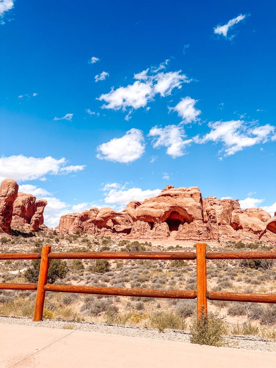 Scenic roadside view of towering red rock formations framed by a wooden fence in Arches National Park.