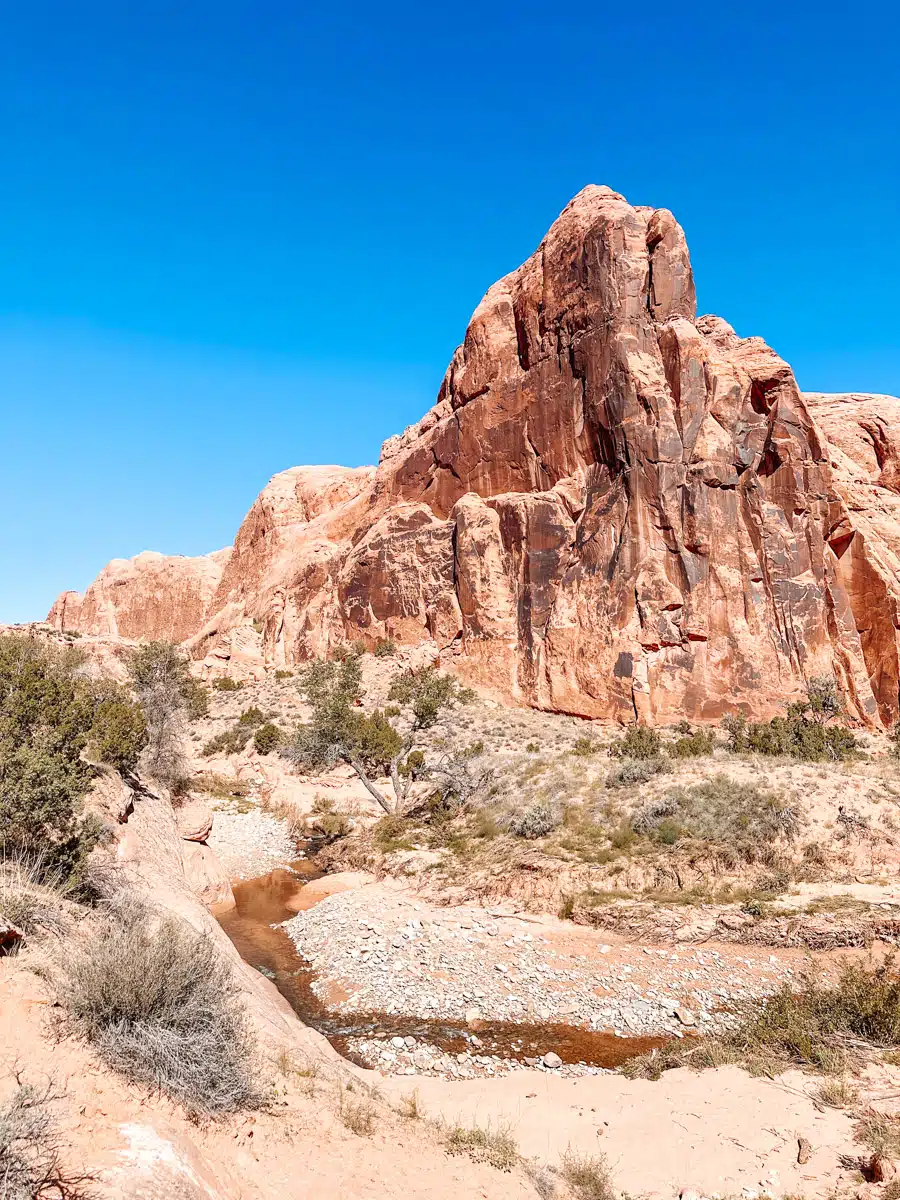 A small stream flows through the desert with a dramatic rock formation in the background, Moab scenery