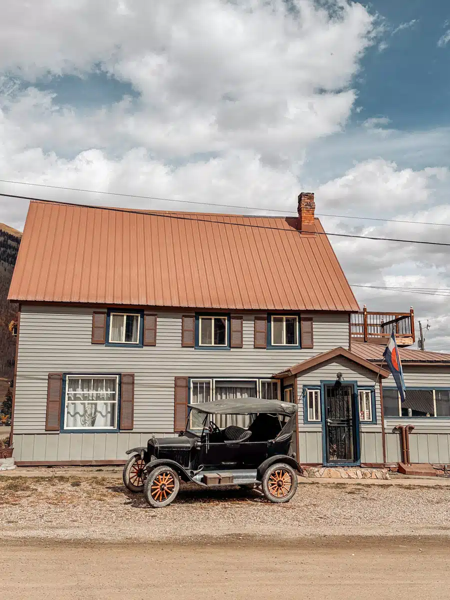 A vintage car parked in front of a charming old house with a Colorado flag, capturing the nostalgic Western vibe of Silverton.