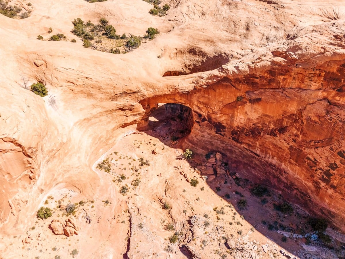 Aerial view of a hidden natural arch carved into orange rock walls, surrounded by desert terrain