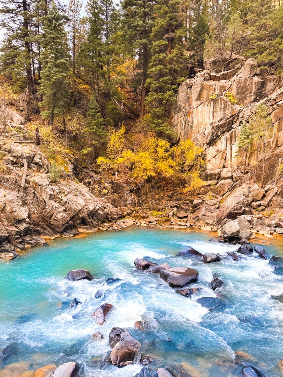 A vibrant turquoise pool of the Animas River surrounded by rocky cliffs and fall foliage in the Colorado mountains.