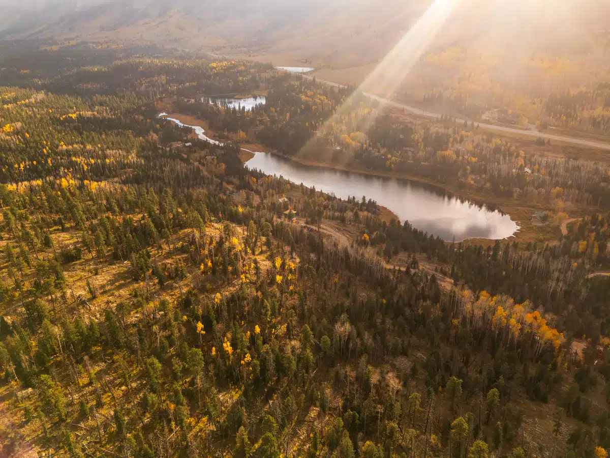 Warm sunset lighting up a forested valley filled with lakes and golden trees in fall.