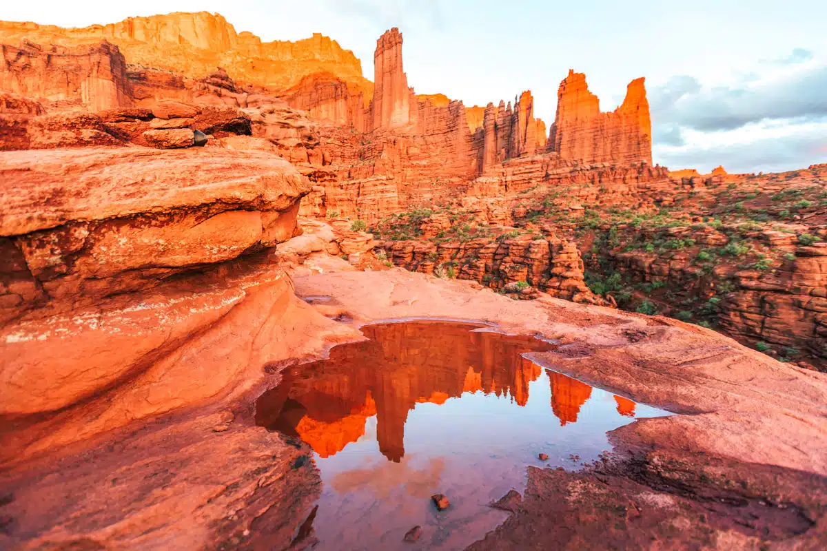Towering red spires of Fisher Towers reflecting in a rock pool at sunset in Moab, Utah