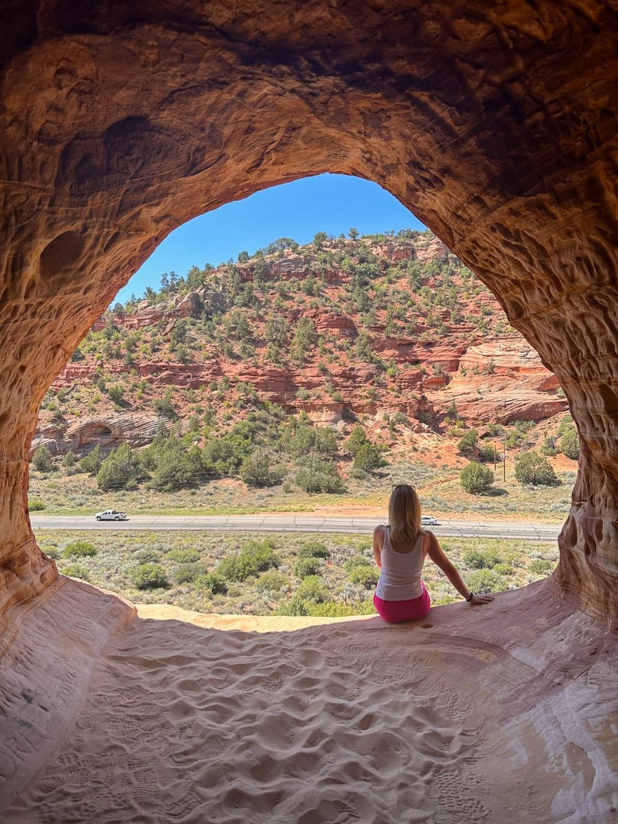 the author's wife sitting on the edge of a cave overlooking the beautiful utah landscape