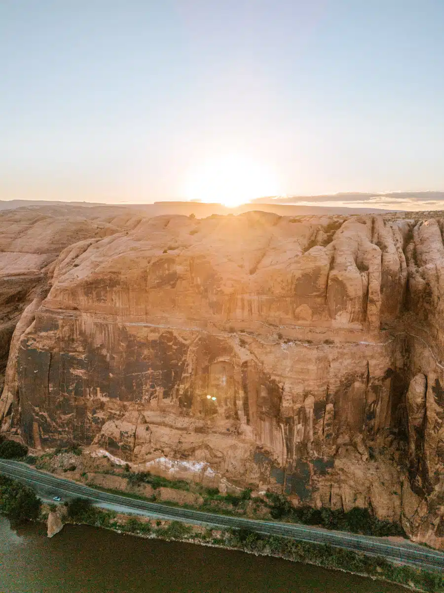 Sun setting behind massive canyon walls with river and road below in Moab, Utah